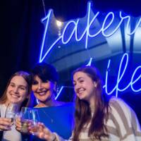 President Mantella smiles and cheers with two grads in front of Laker for a Lifetime sign